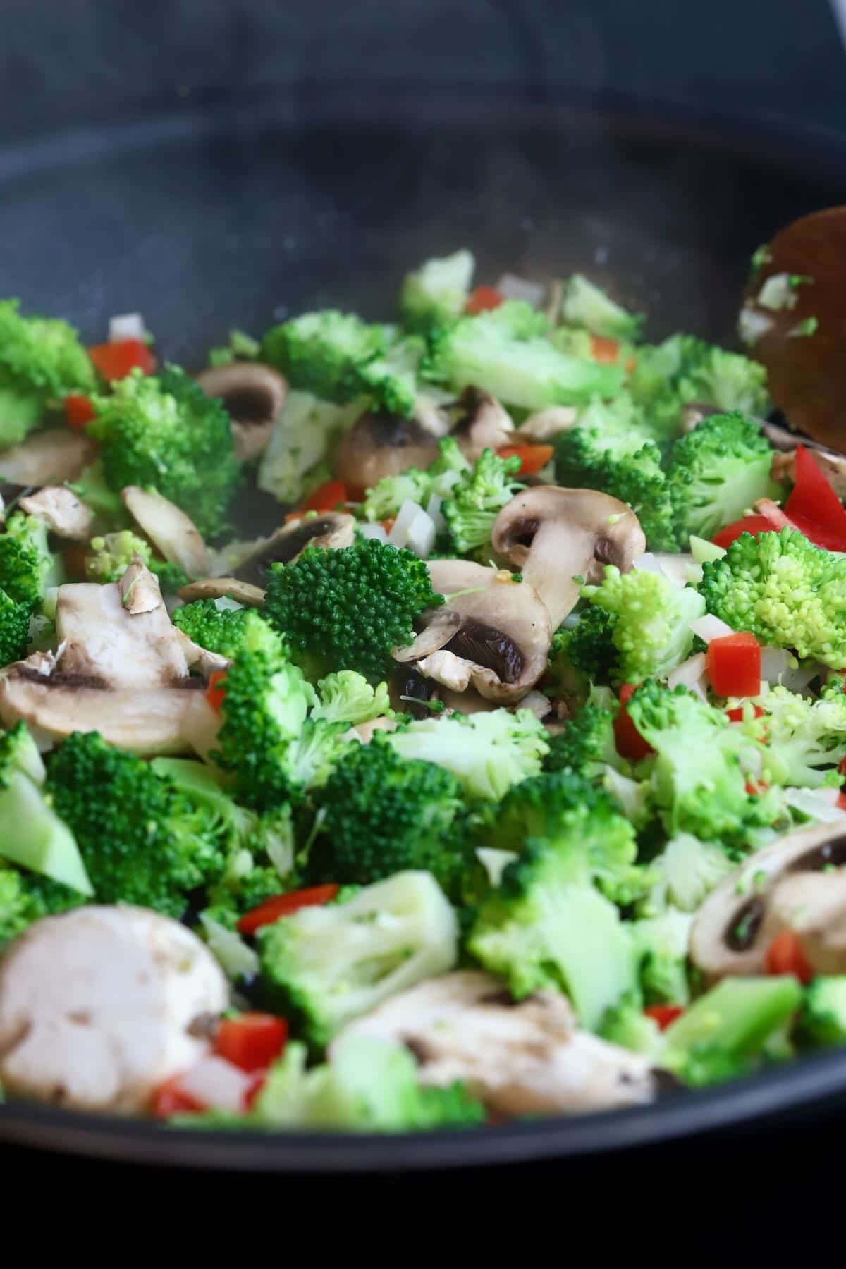 Broccoli, mushrooms, and red pepper cooking in a skillet. 