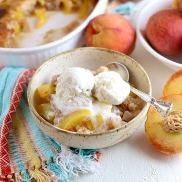 A bowl of peach cobbler topped with ice cream.