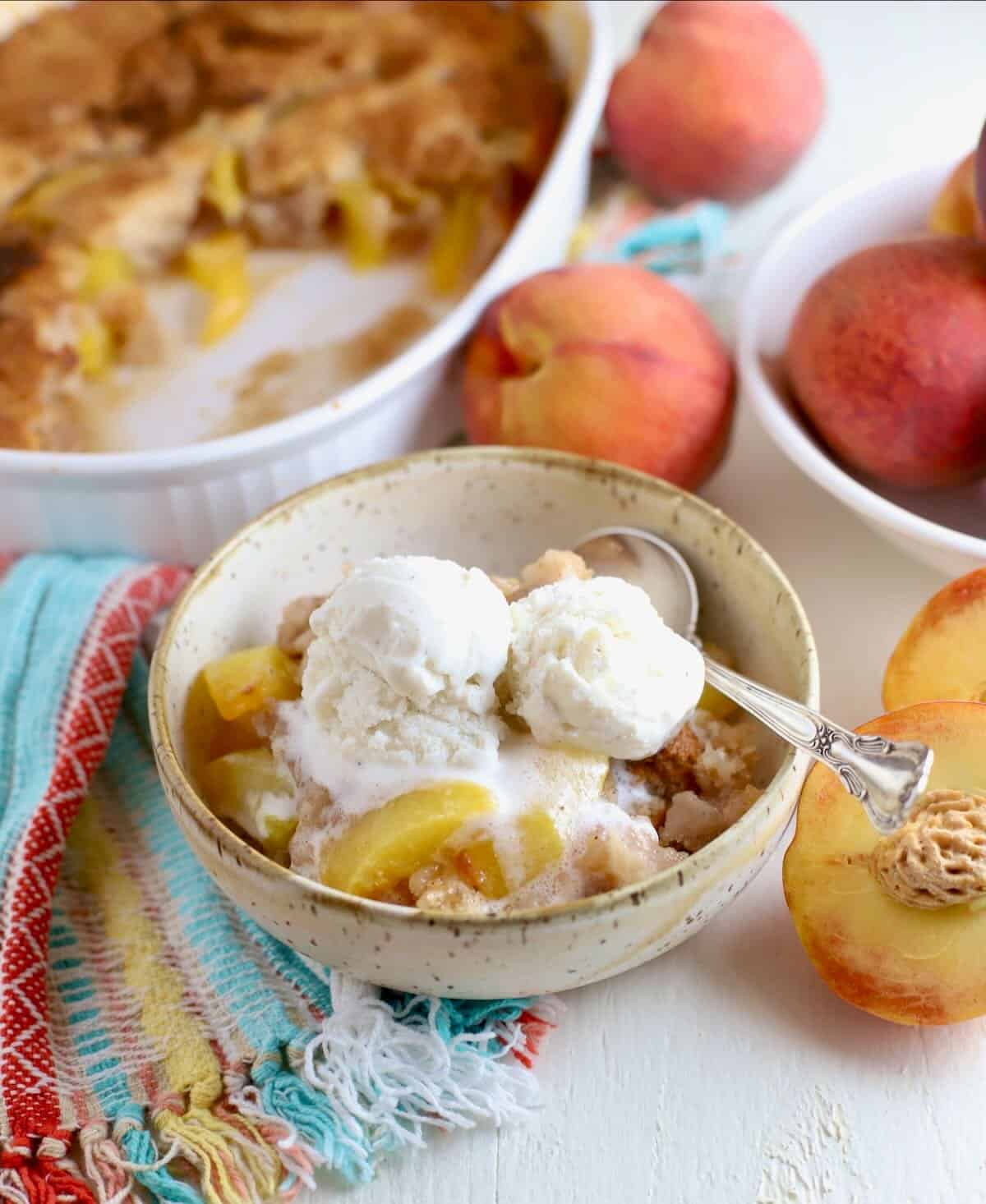 A bowl of peach cobbler topped with two scoops of vanilla ice cream. 
