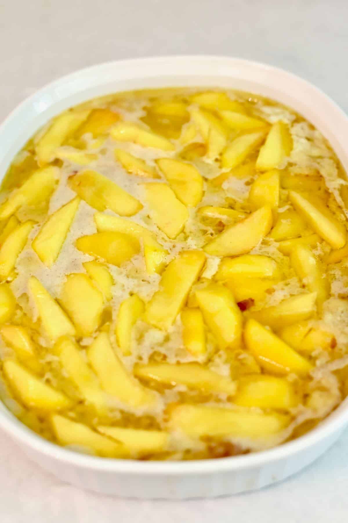 Sliced peaches with batter in a baking dish ready for the oven.