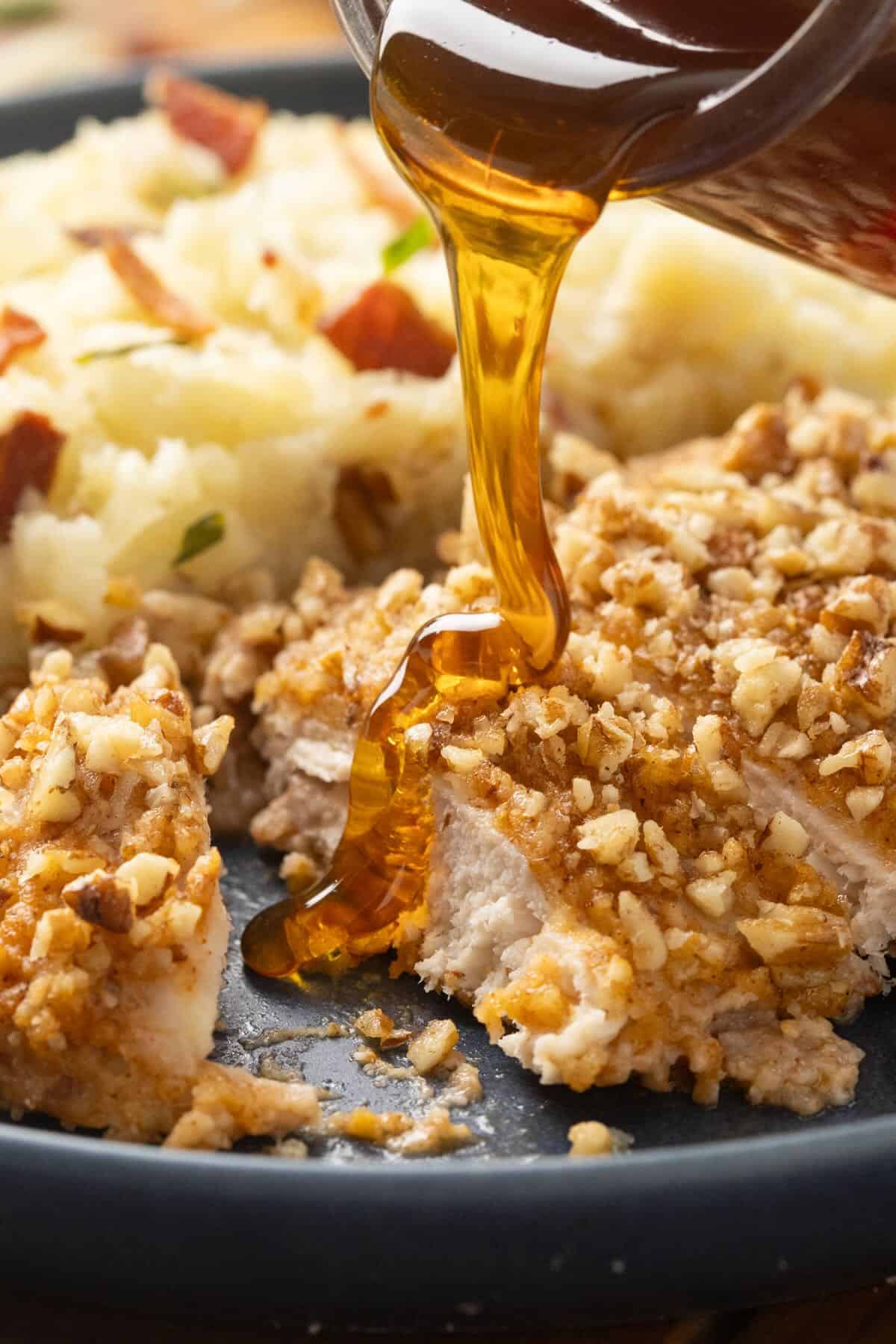 Pecan crusted chicken with hot honey being poured over it.