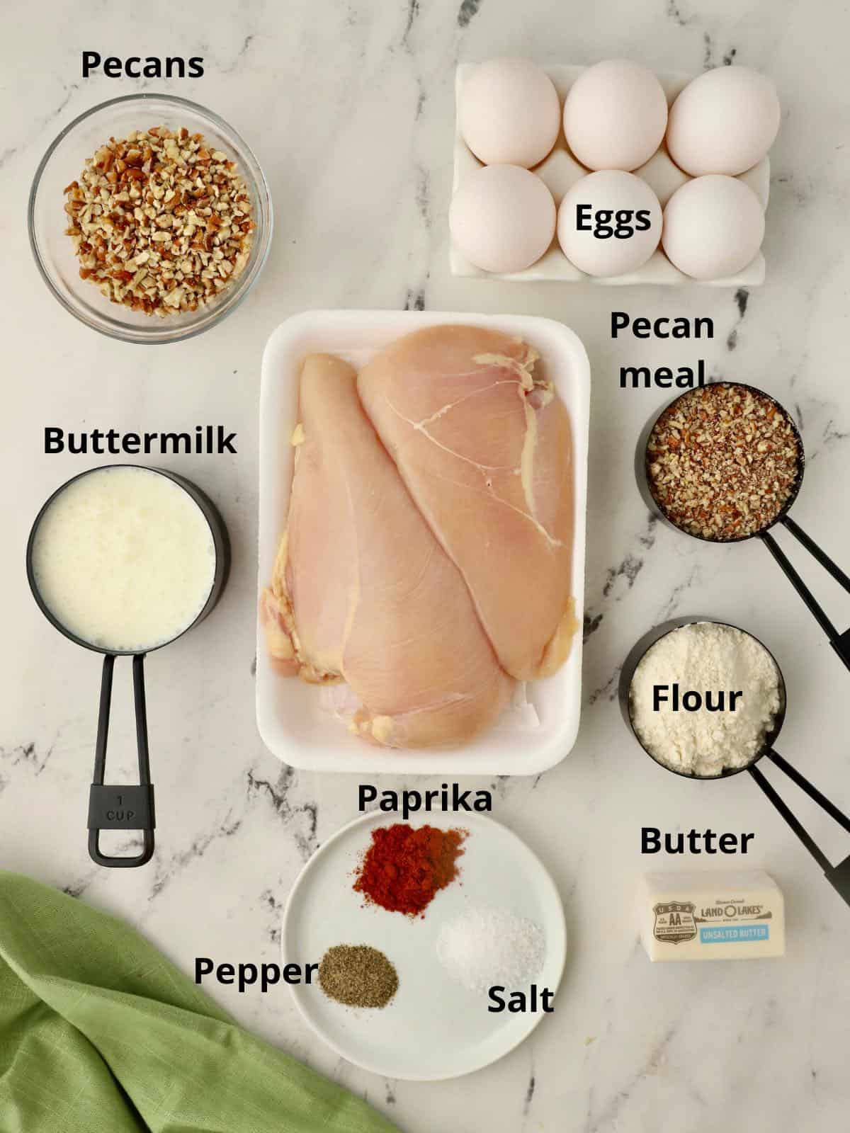 Raw chicken breasts and other ingredients to make pecan crusted chicken. 