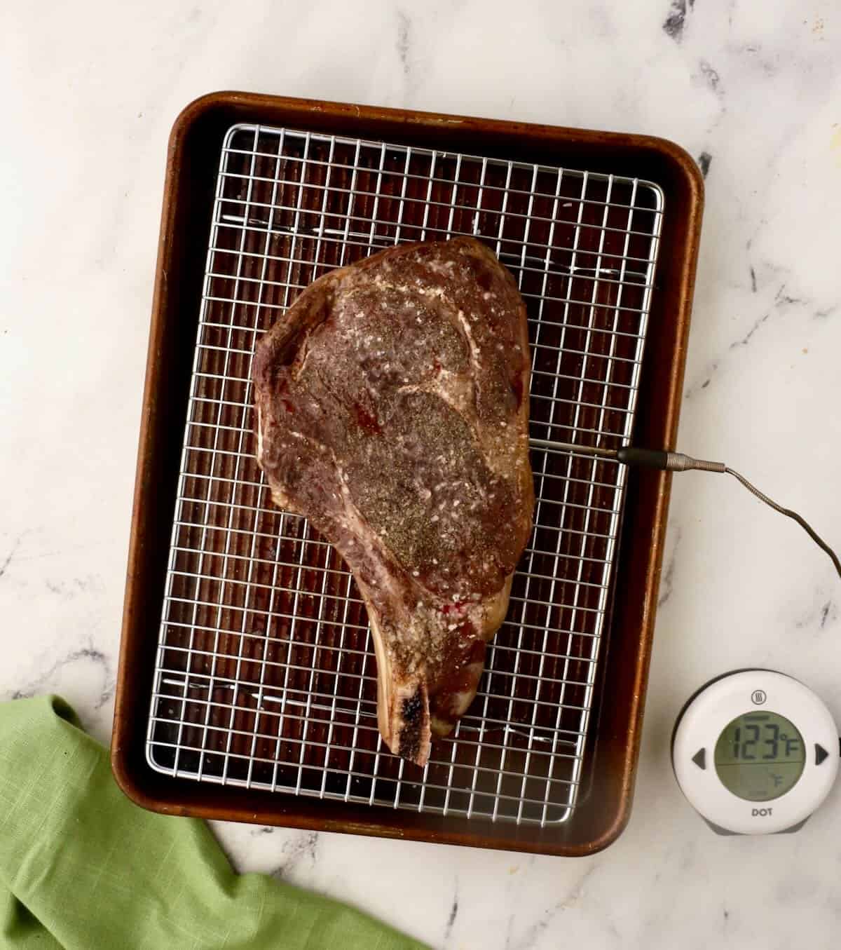 A reverse seared ribeye steak on a wire rack with a meat thermometer. 