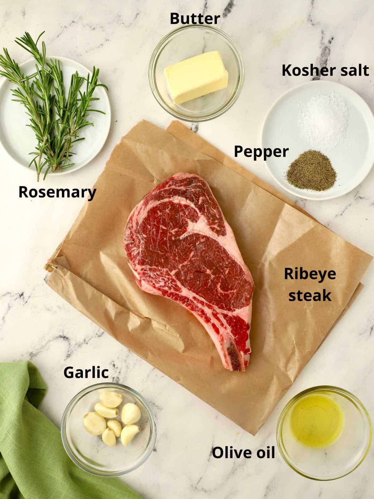 A raw steak, garlic, rosemary and other seasonings. 