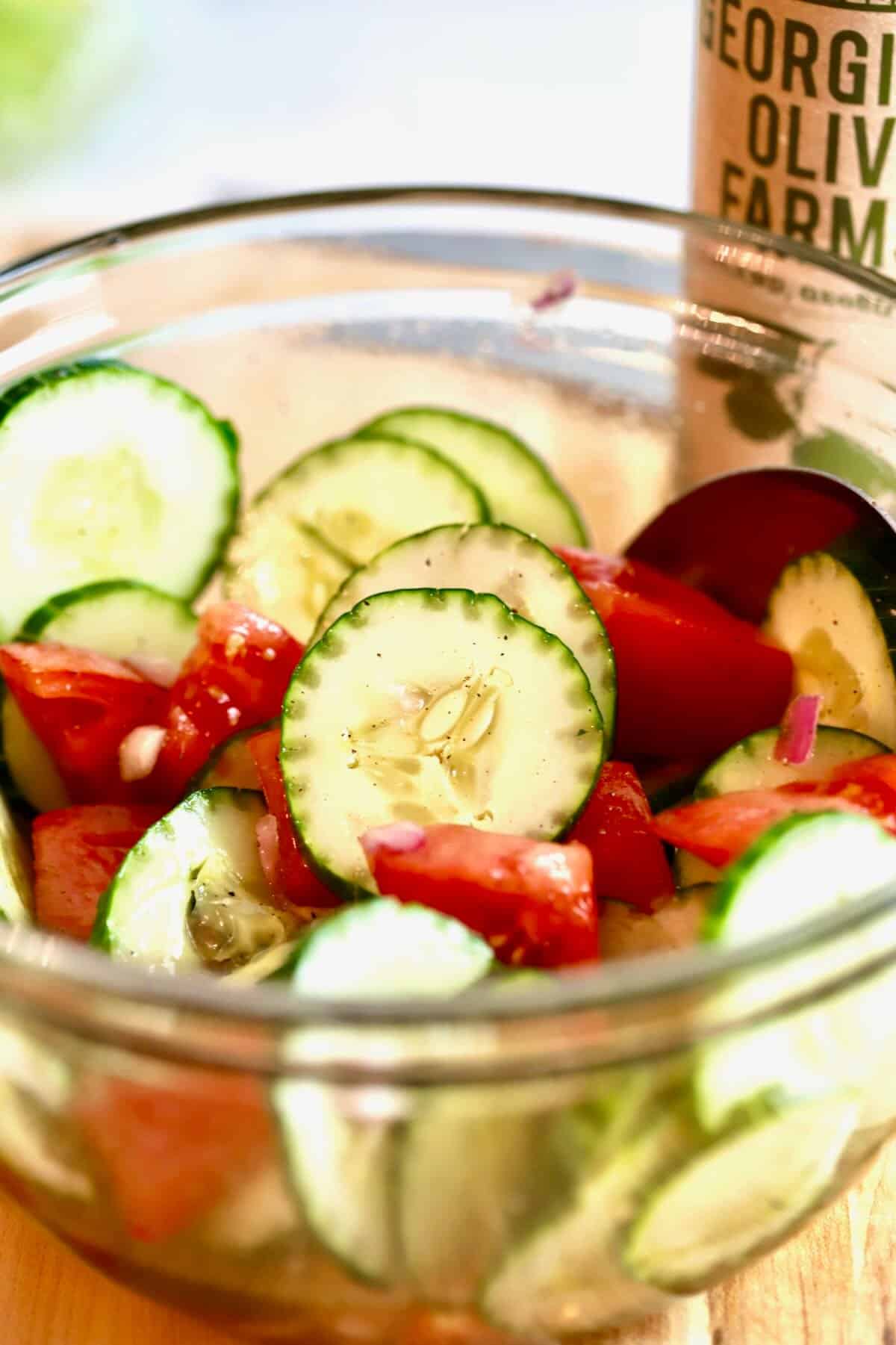 Sliced cucumbers, tomatoes and onions topped with salad dressing in a bowl. 