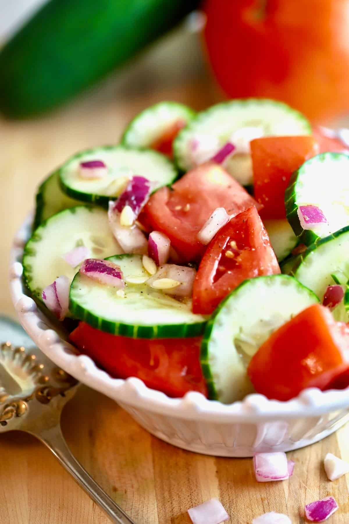 A white bowl full of cucumber and tomato salad. 