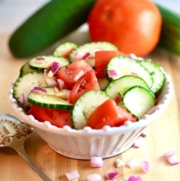 Sliced cucumbers, tomatoes and onion in a white bowl.