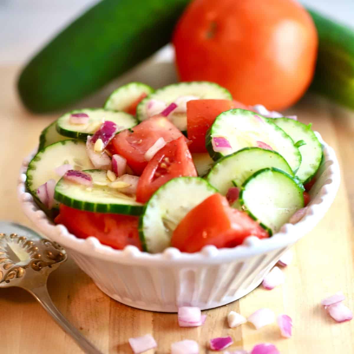Sliced cucumbers, tomatoes and onion in a white bowl.