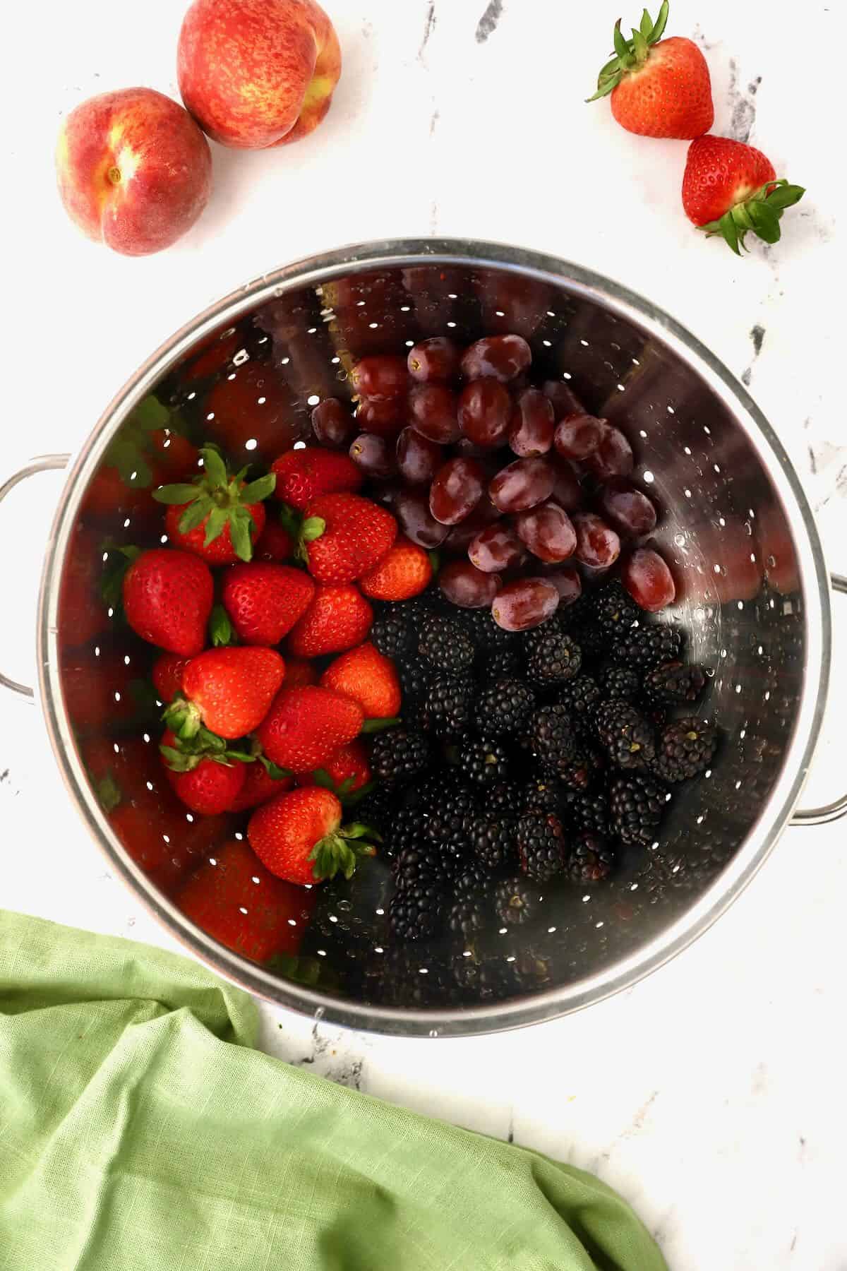 A colander with strawberries, grapes and blackberries. 