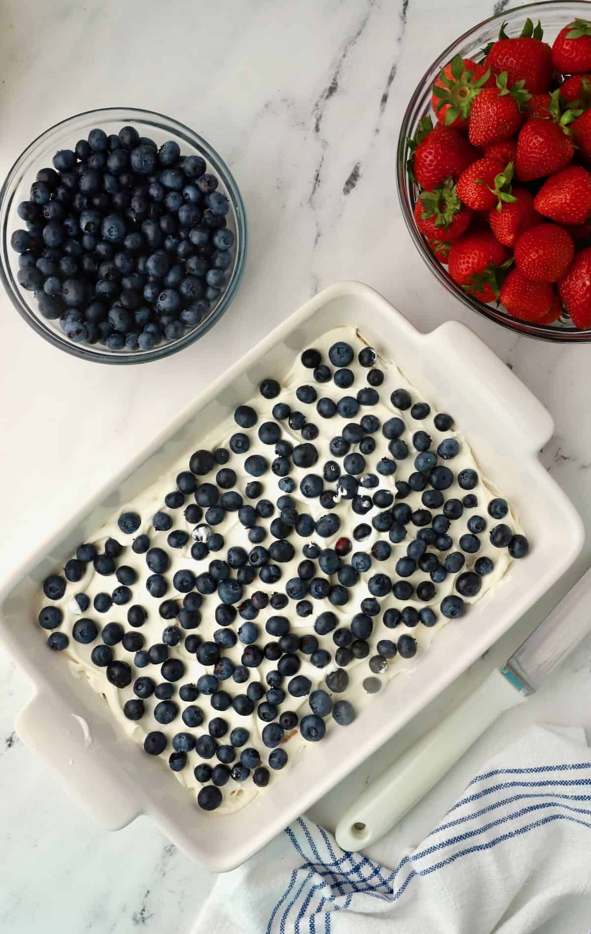 A layer of blueberries over a layer of whipped cream in a baking dish. 