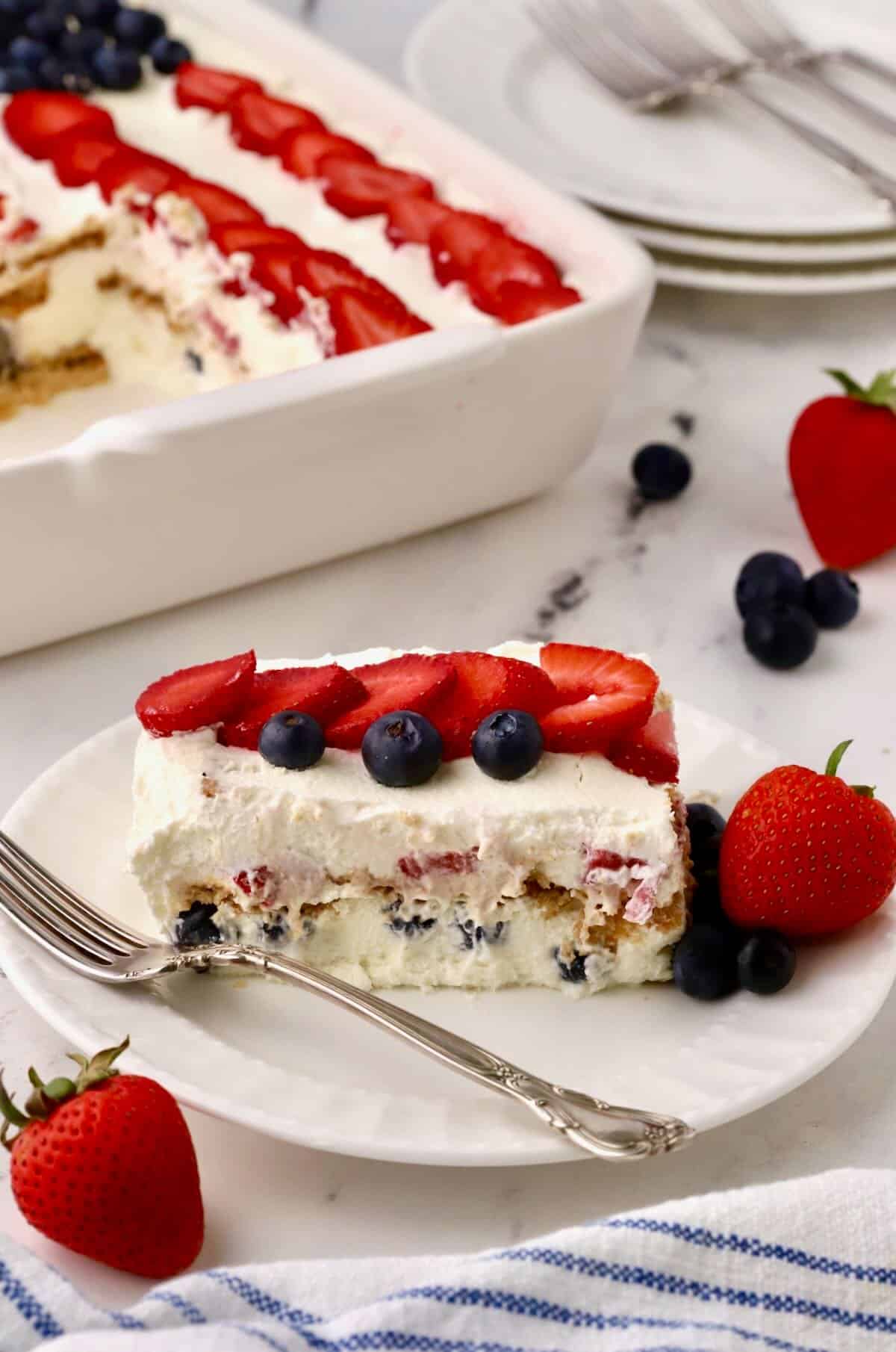 A slice of icebox cake topped with sliced strawberries and blueberries. 