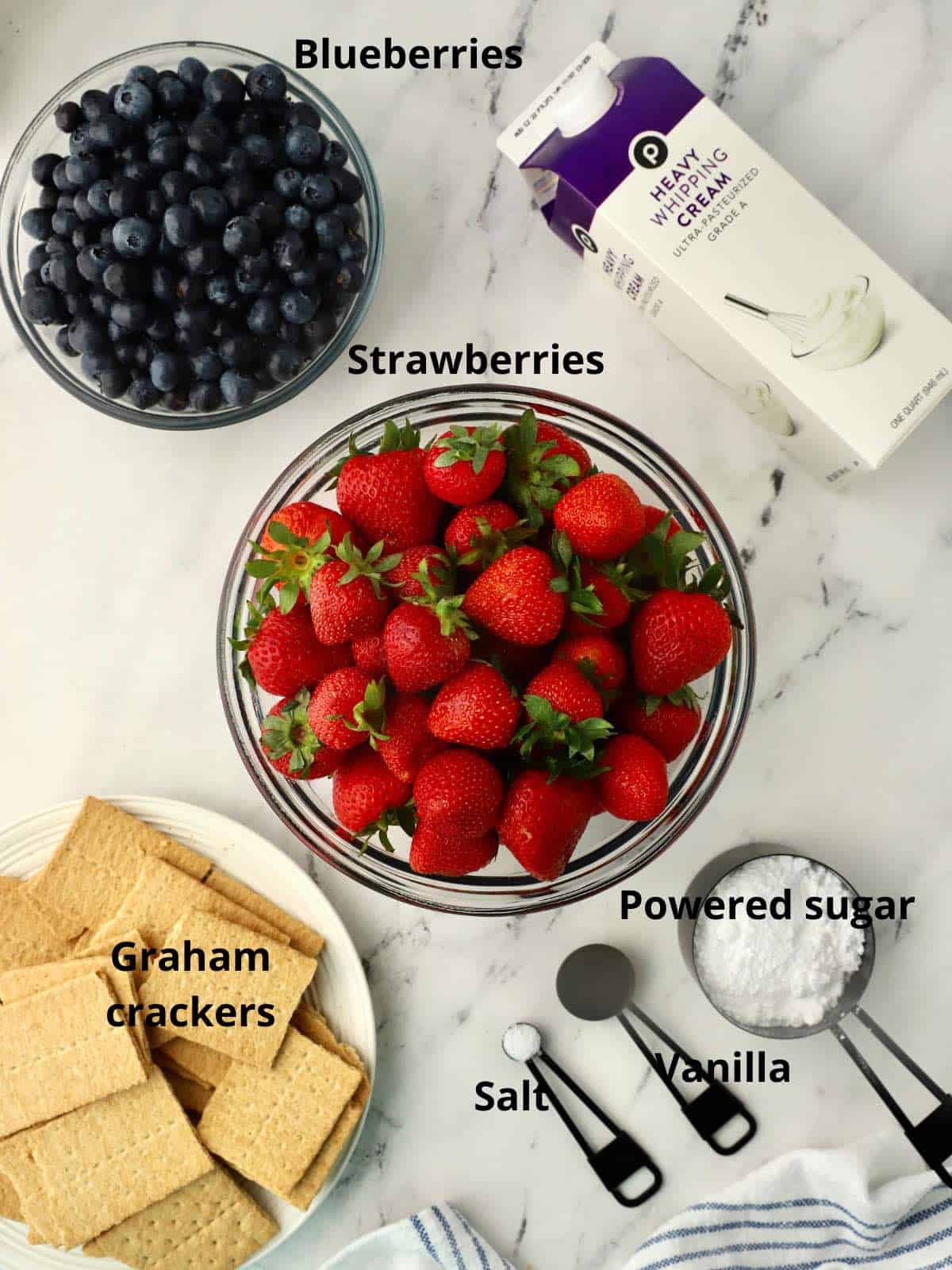 A bowl of fresh strawberries, along with blueberries and other ingredients for an icebox cake. 