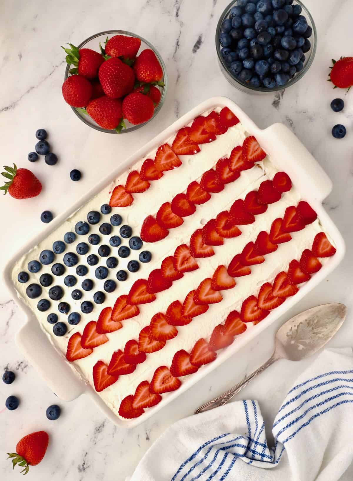 An ice box cake topped with whipped cream , strawberries and blueberries that looks like a flag. 