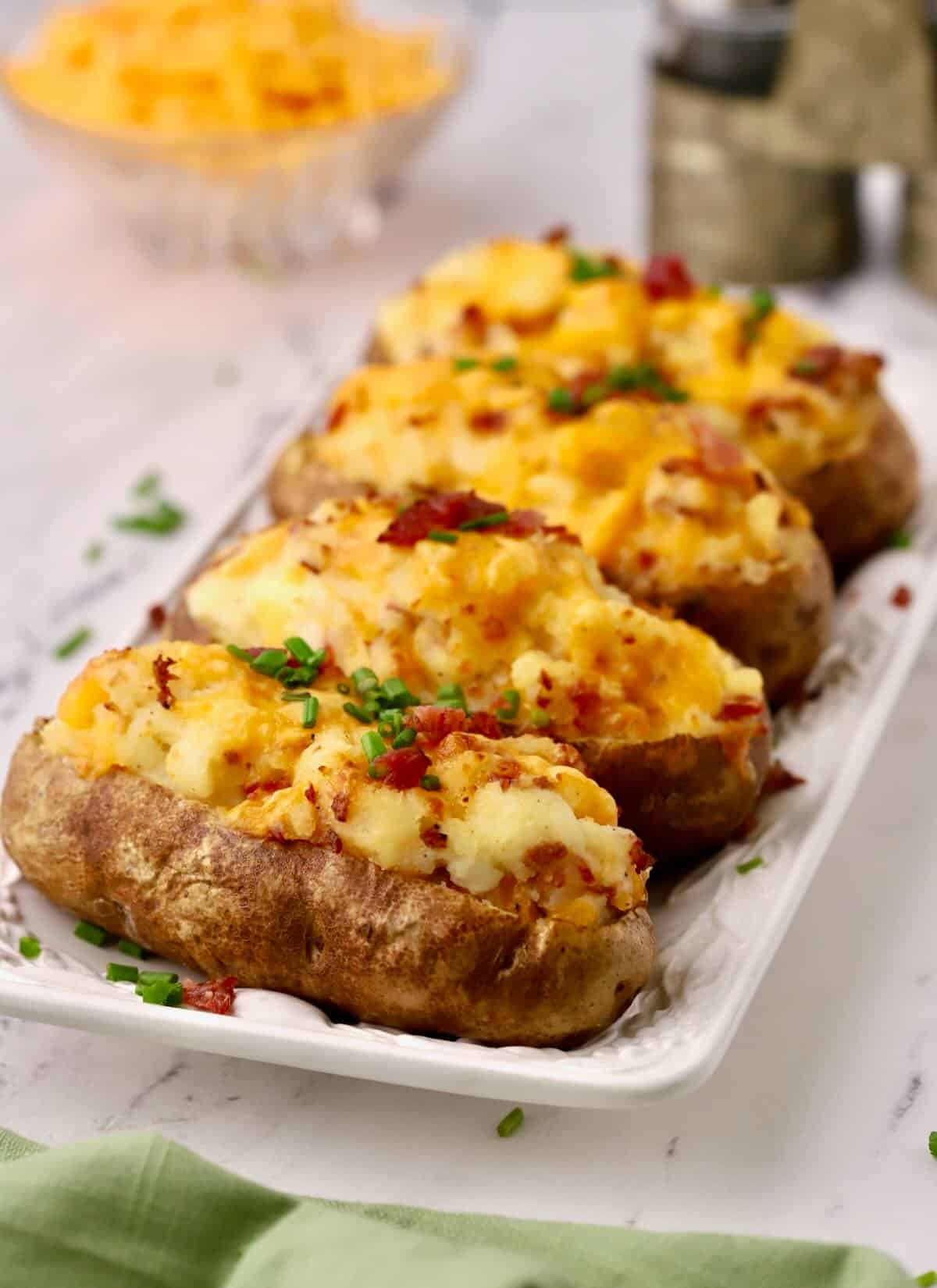 Four twice baked potatoes on a white serving dish. 