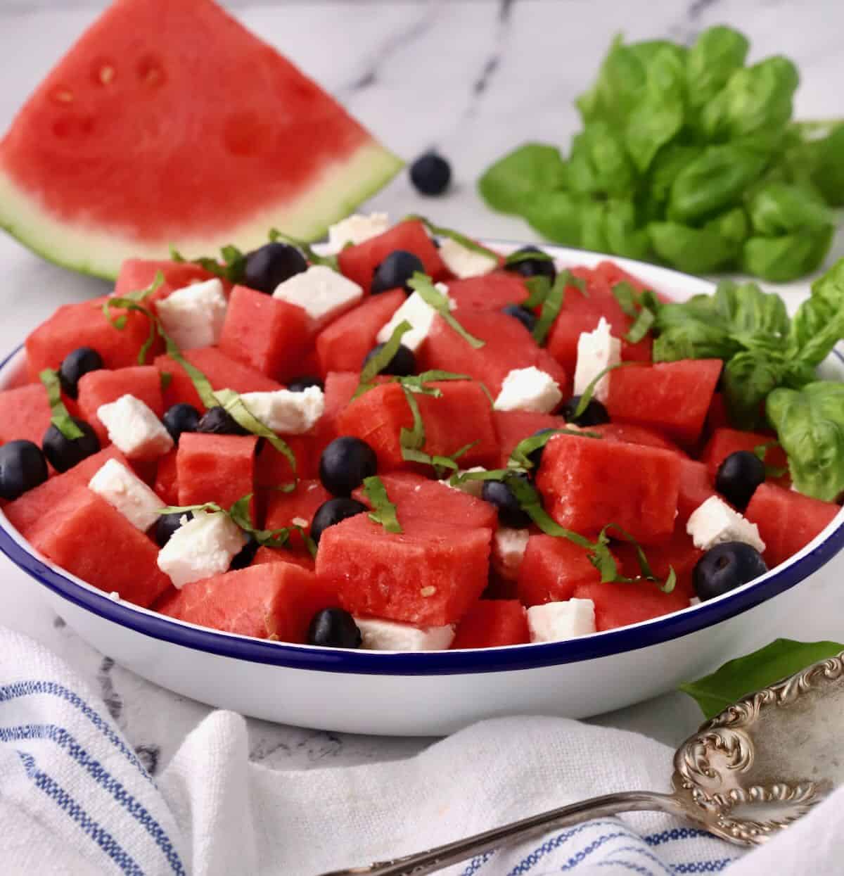 A blue and white metal bowl full of watermelon feta salad with blueberries.. 