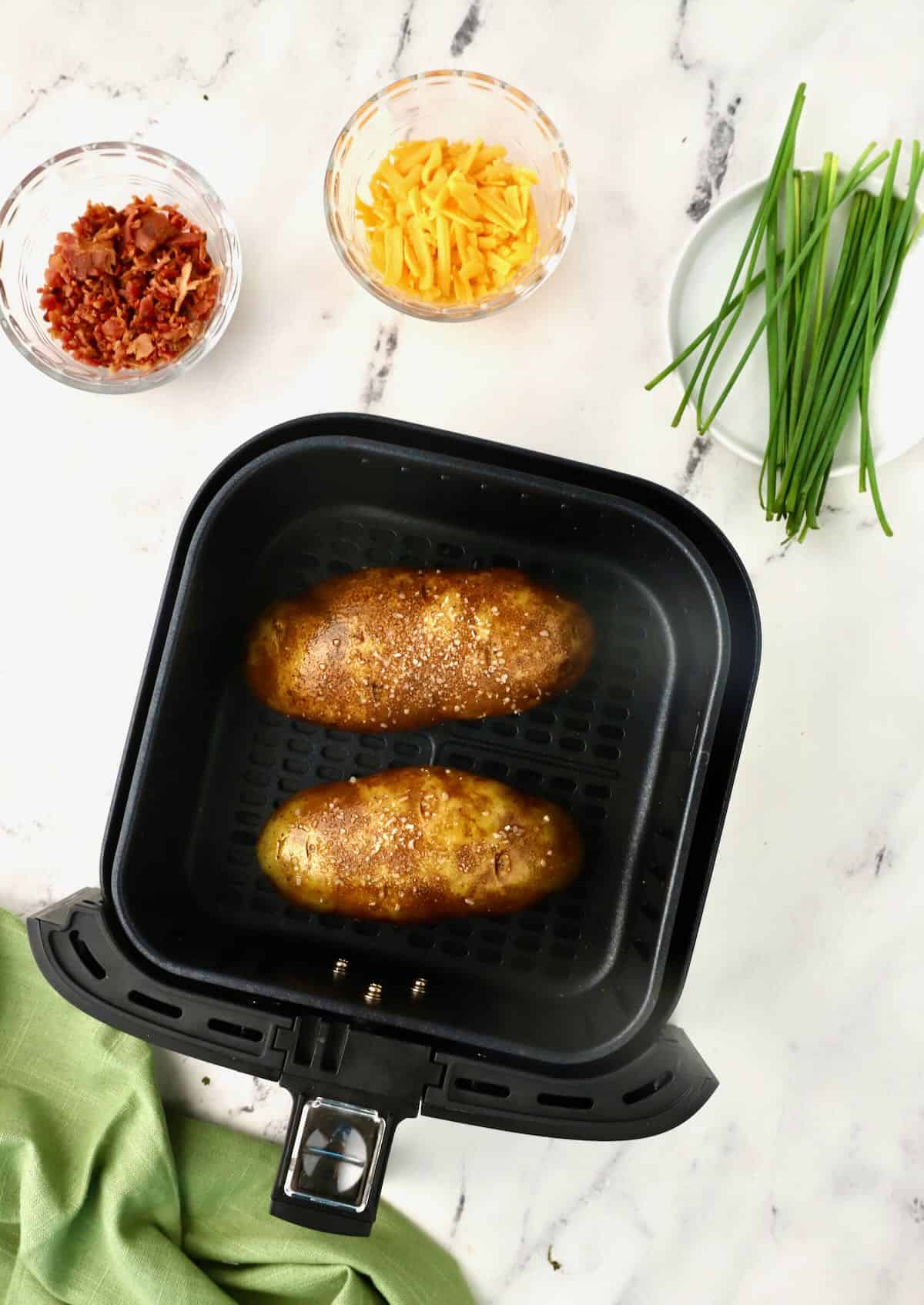 Two potatoes in the basket of an air fryer. 