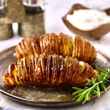 Two hasselback potatoes on a plate garnished with a spring of rosemary.