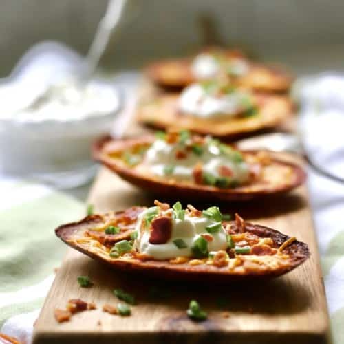 Potato skins topped with sour cream on a cutting board.