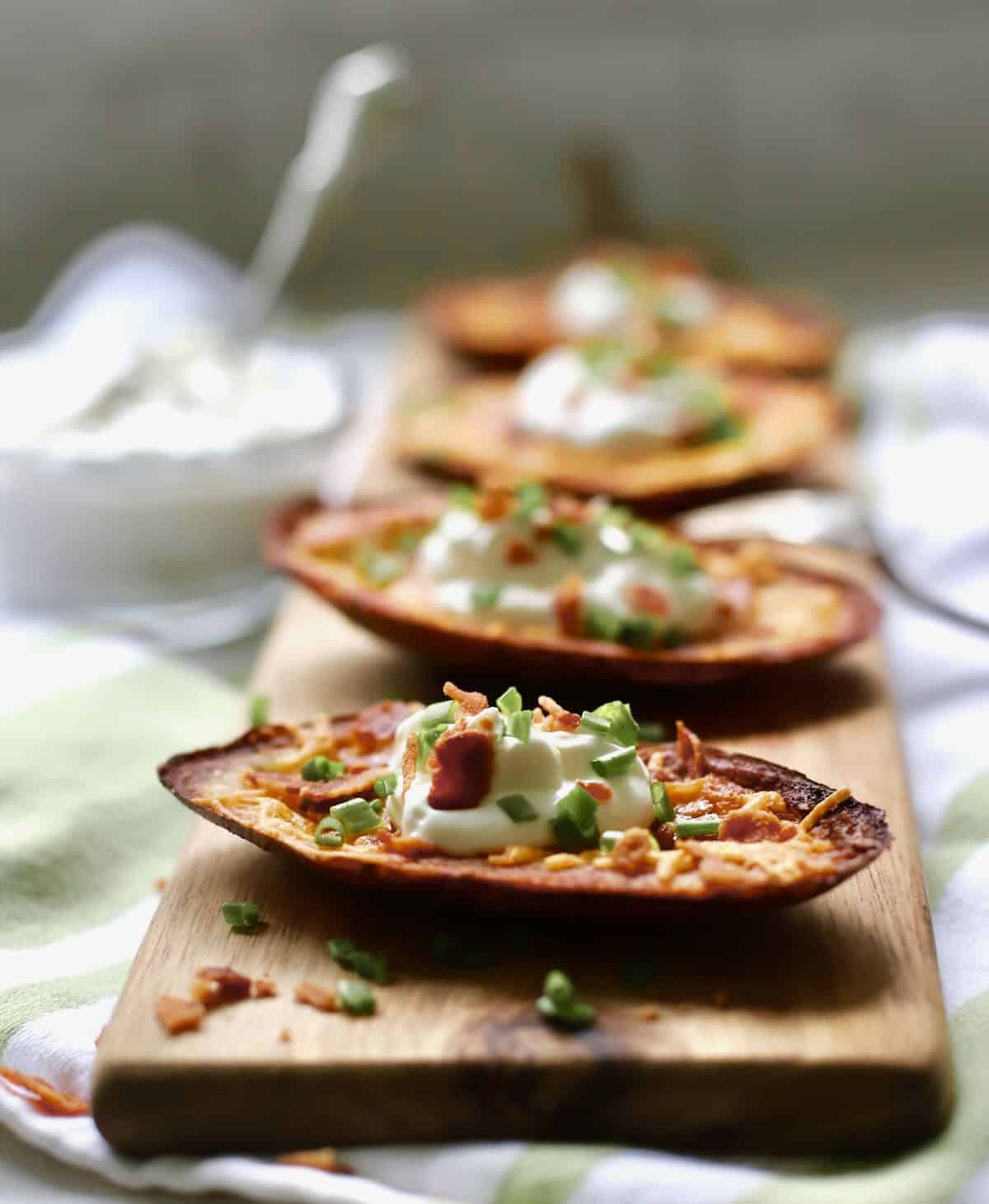 Four air fried potato skins topped with sour cream on a cutting board. 