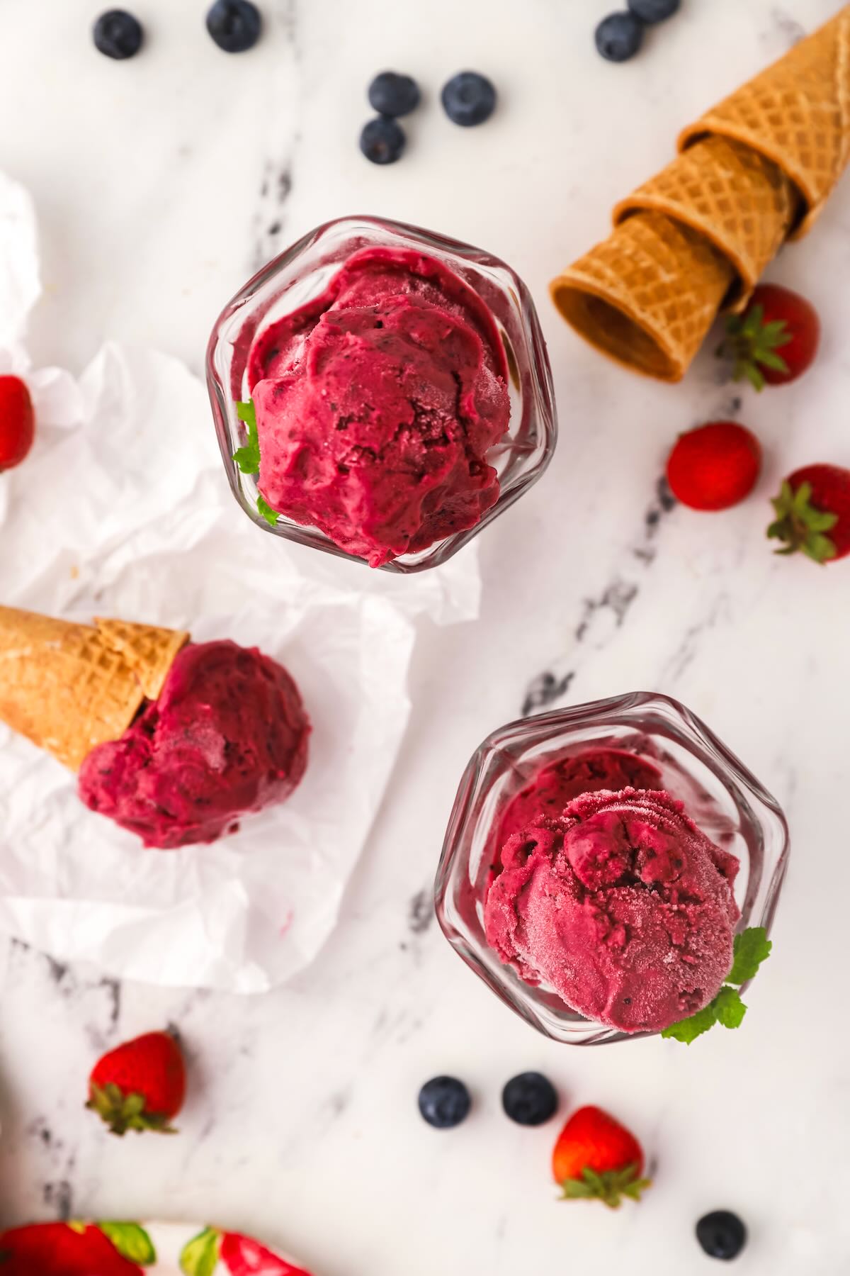 Two dessert dishes with berry sherbet and one ice cream cone. 