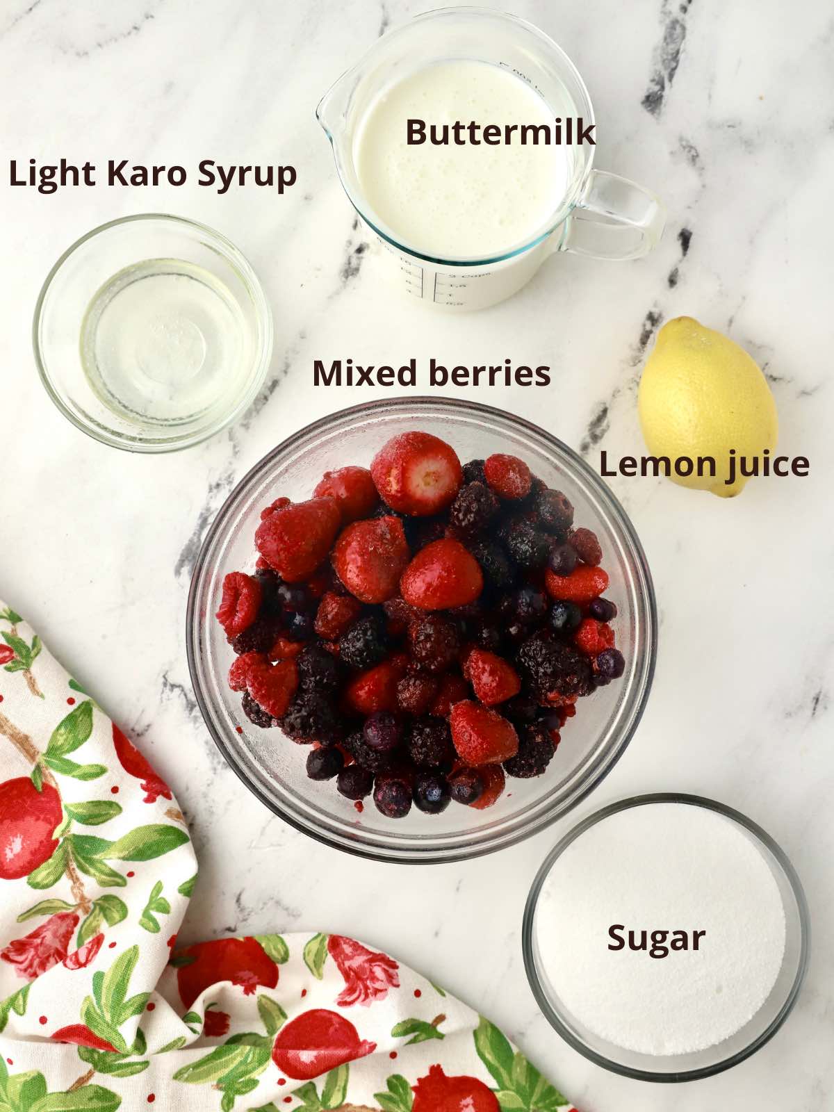 A large glass bowl of mixed berries, plus sugar, buttermilk and a lemon. 