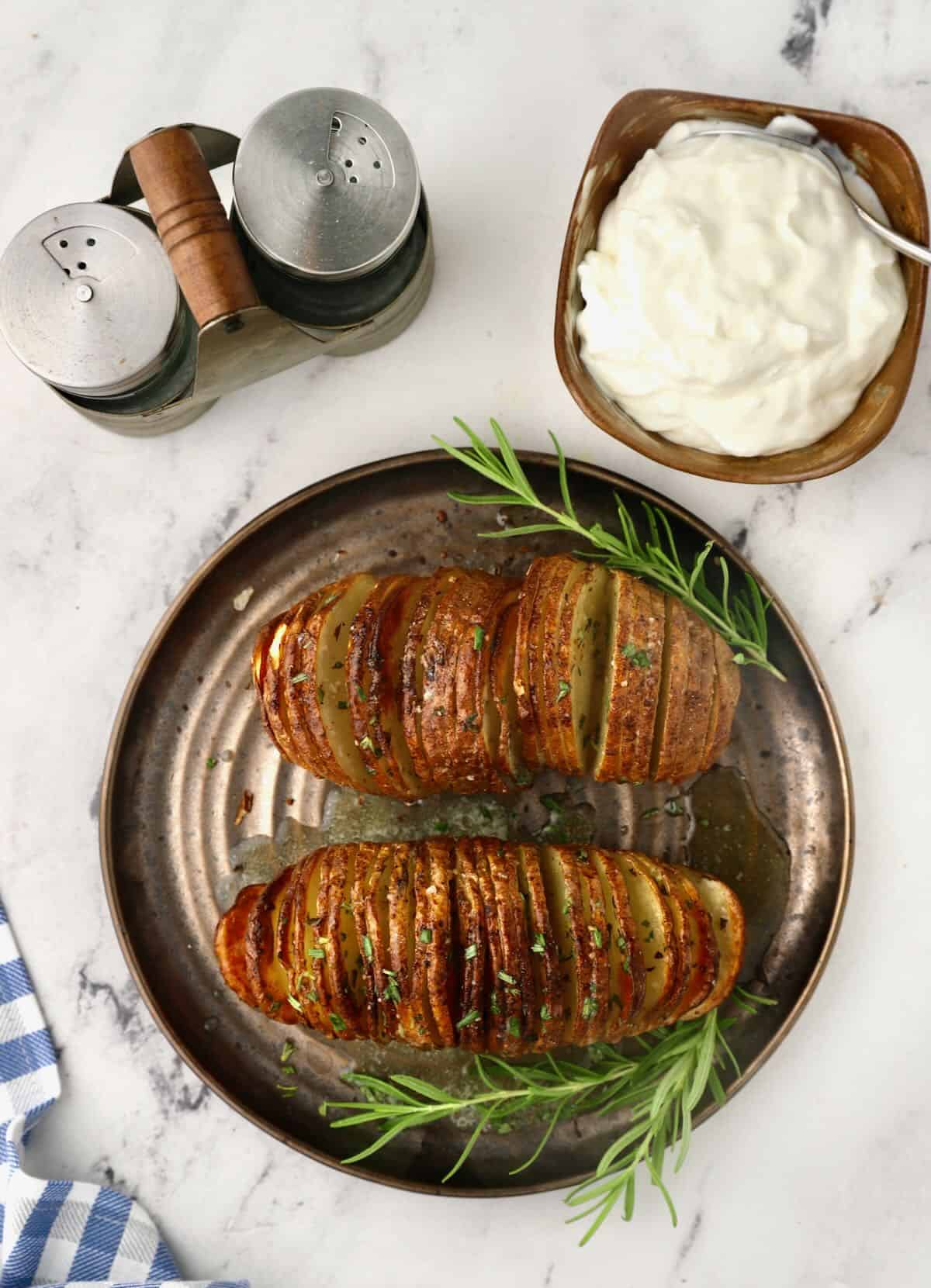 Two hasselback potatoes on a plate with a bowl of sour cream. 