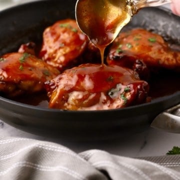 Honey baked chicken thighs in a cast iron skillet being topped with a honey glaze.