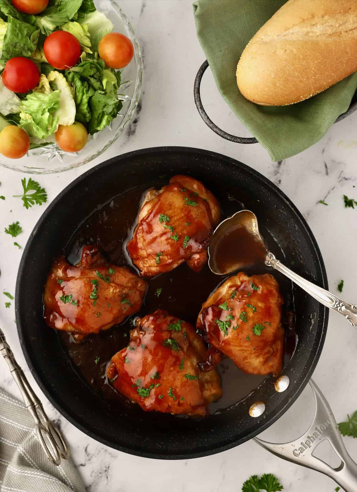 Spooning honey glaze over baked chicken thighs in a skillet. 