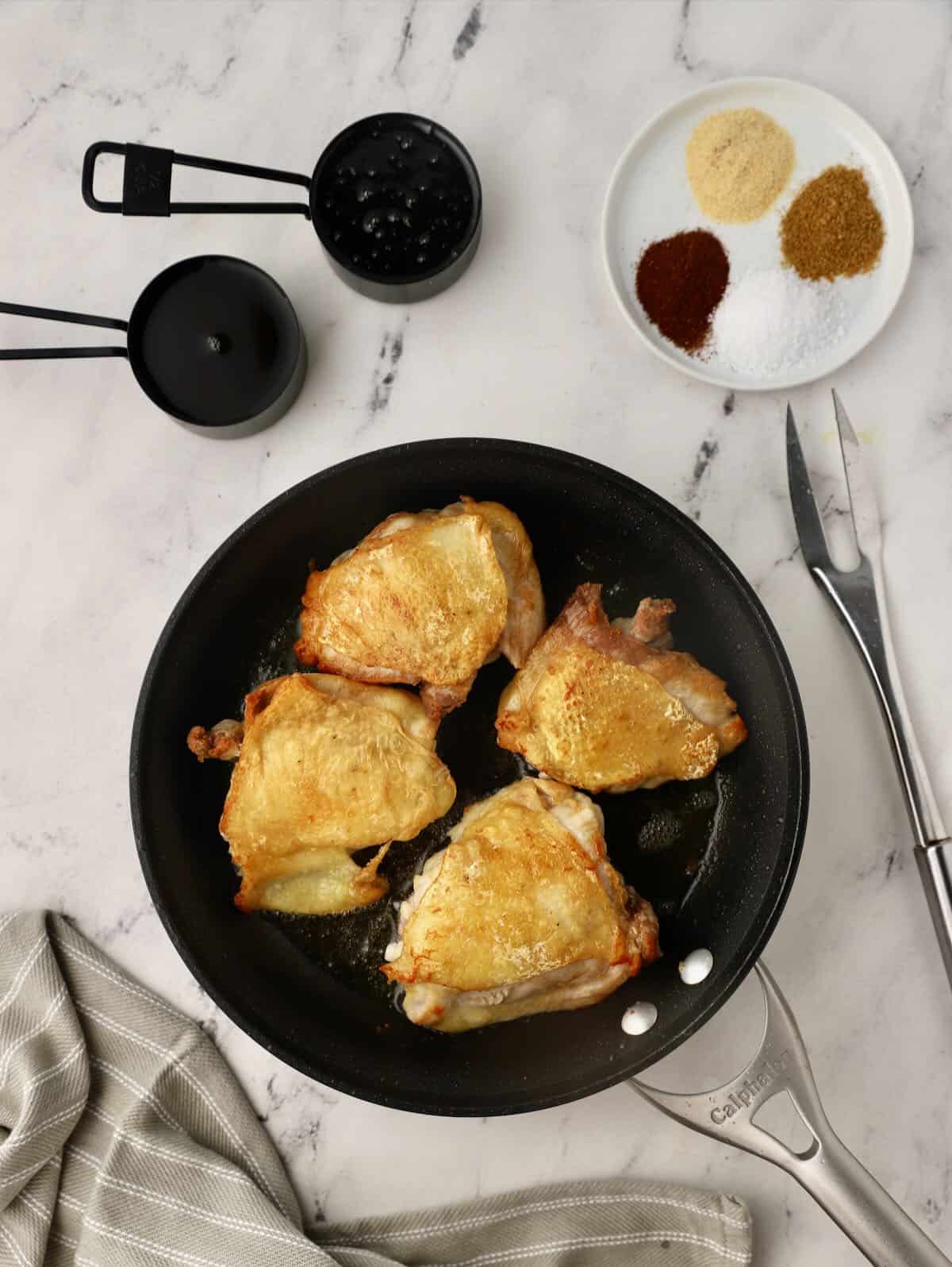 Chicken thighs being pan-seared in a skillet. 