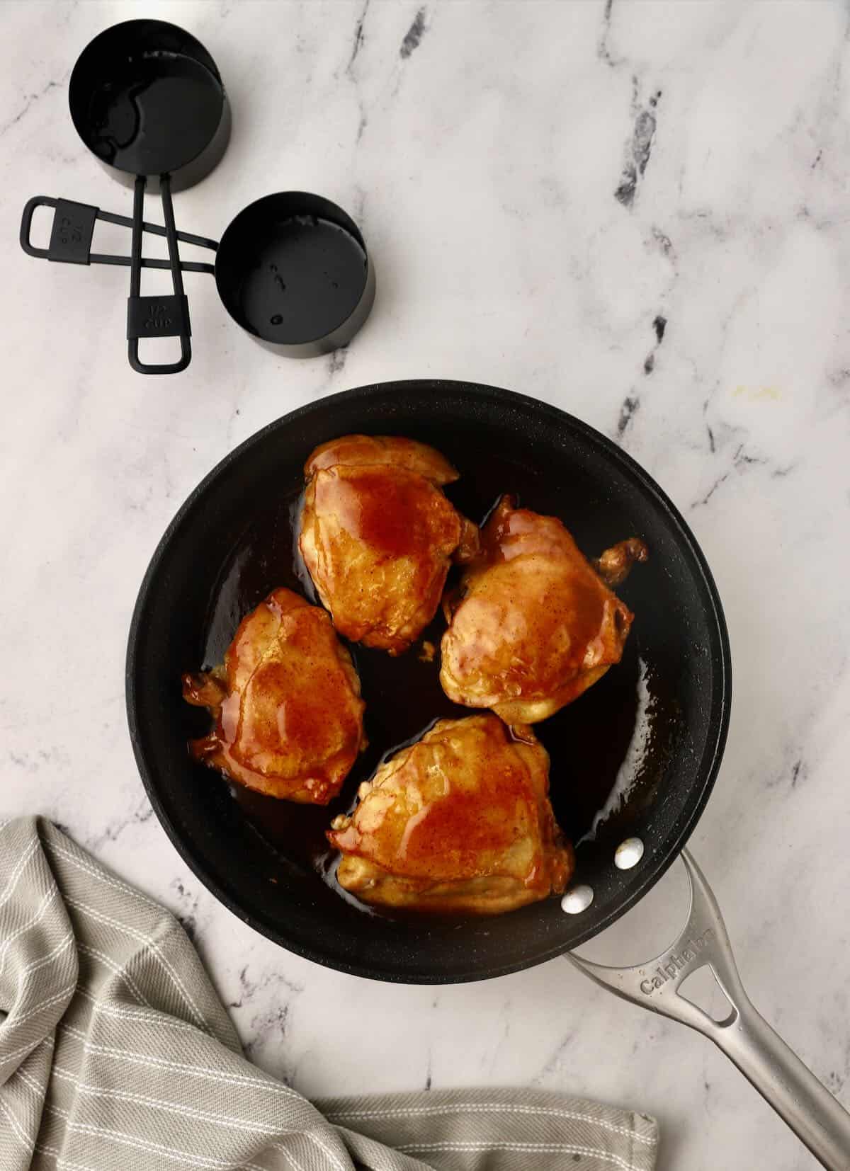 Chicken thighs covered in a honey glaze cooking in a skillet. 