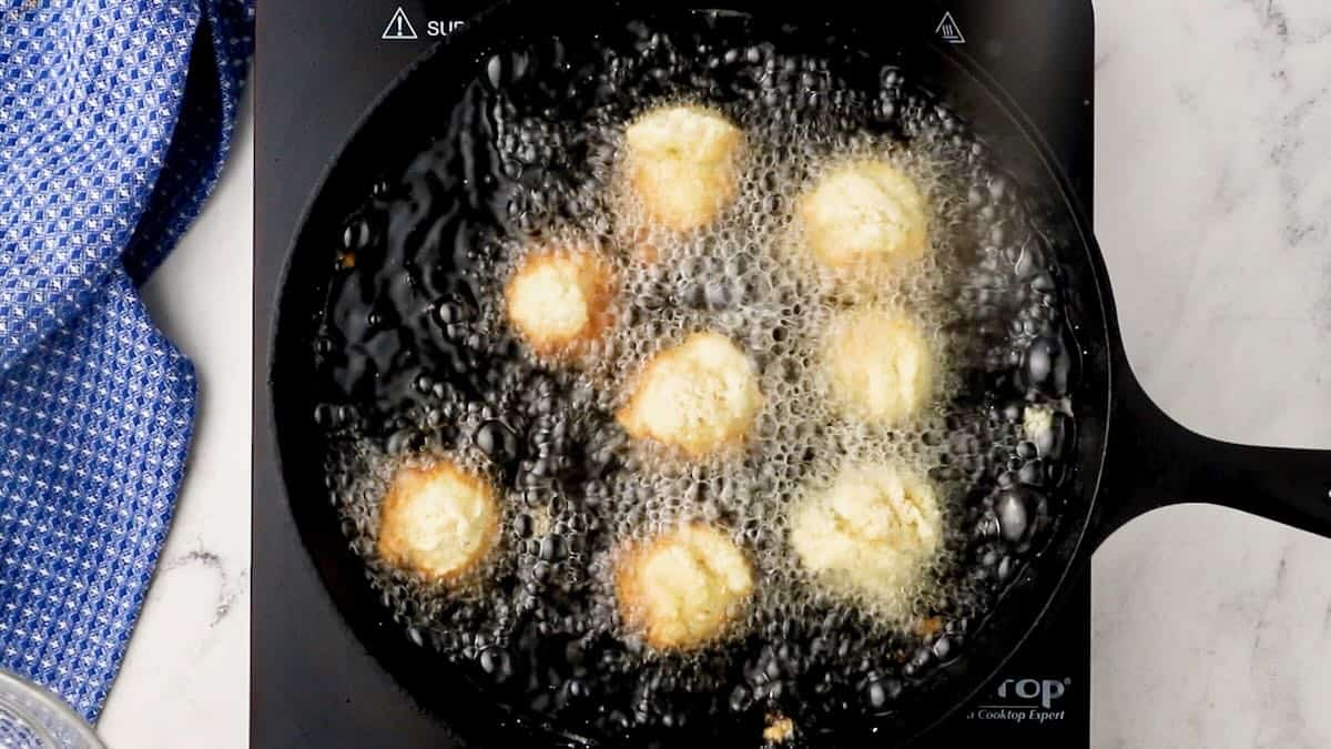 Hush puppies frying in a cast iron skillet. 