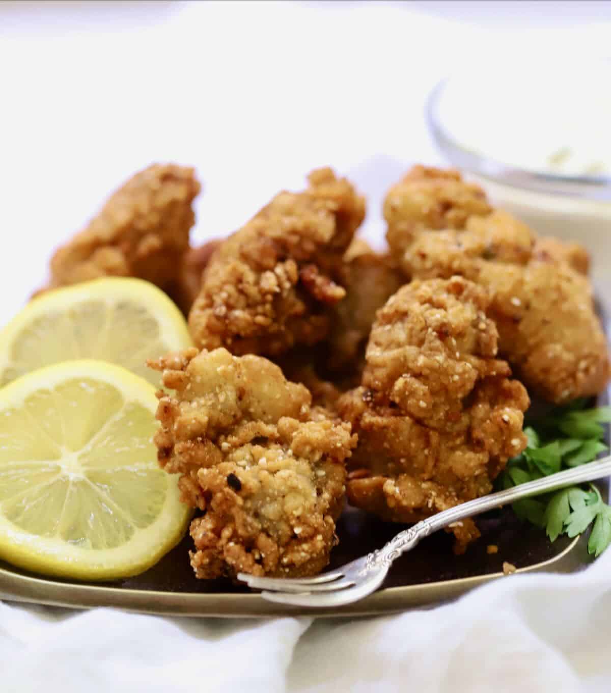 Fried oysters on a plate garnished with lemon slices.
