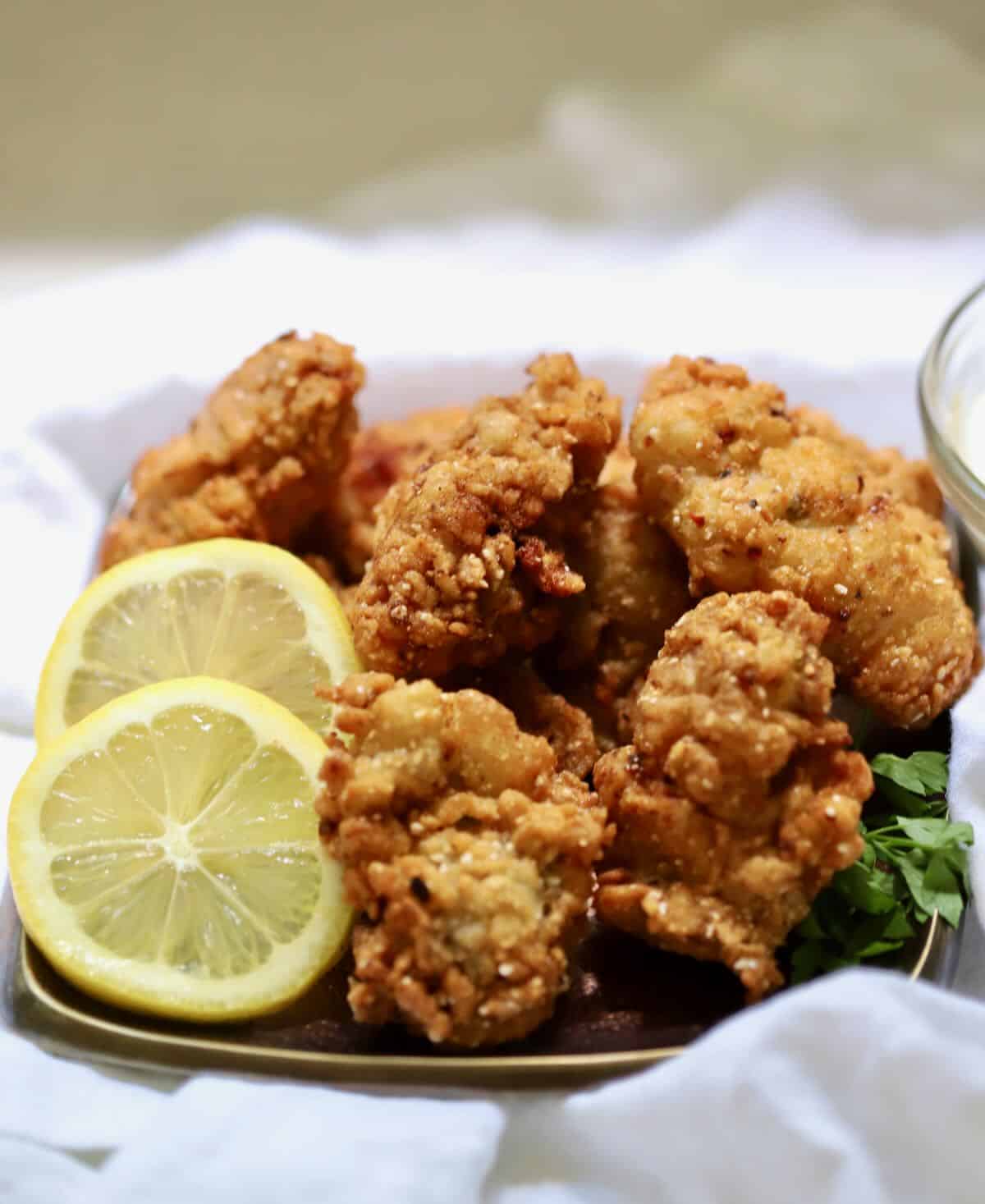 Fried oysters on a bronze plate garnished with lemon slices. 