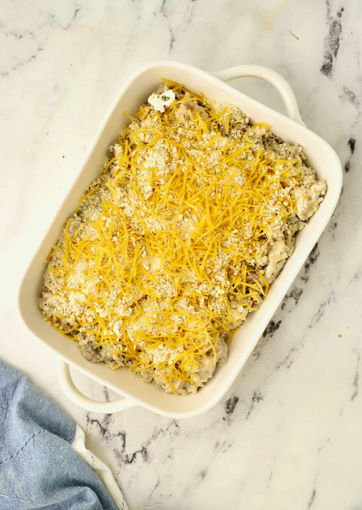 A baking dish with a chicken and rice casserole topped with cheese ready for the oven. 