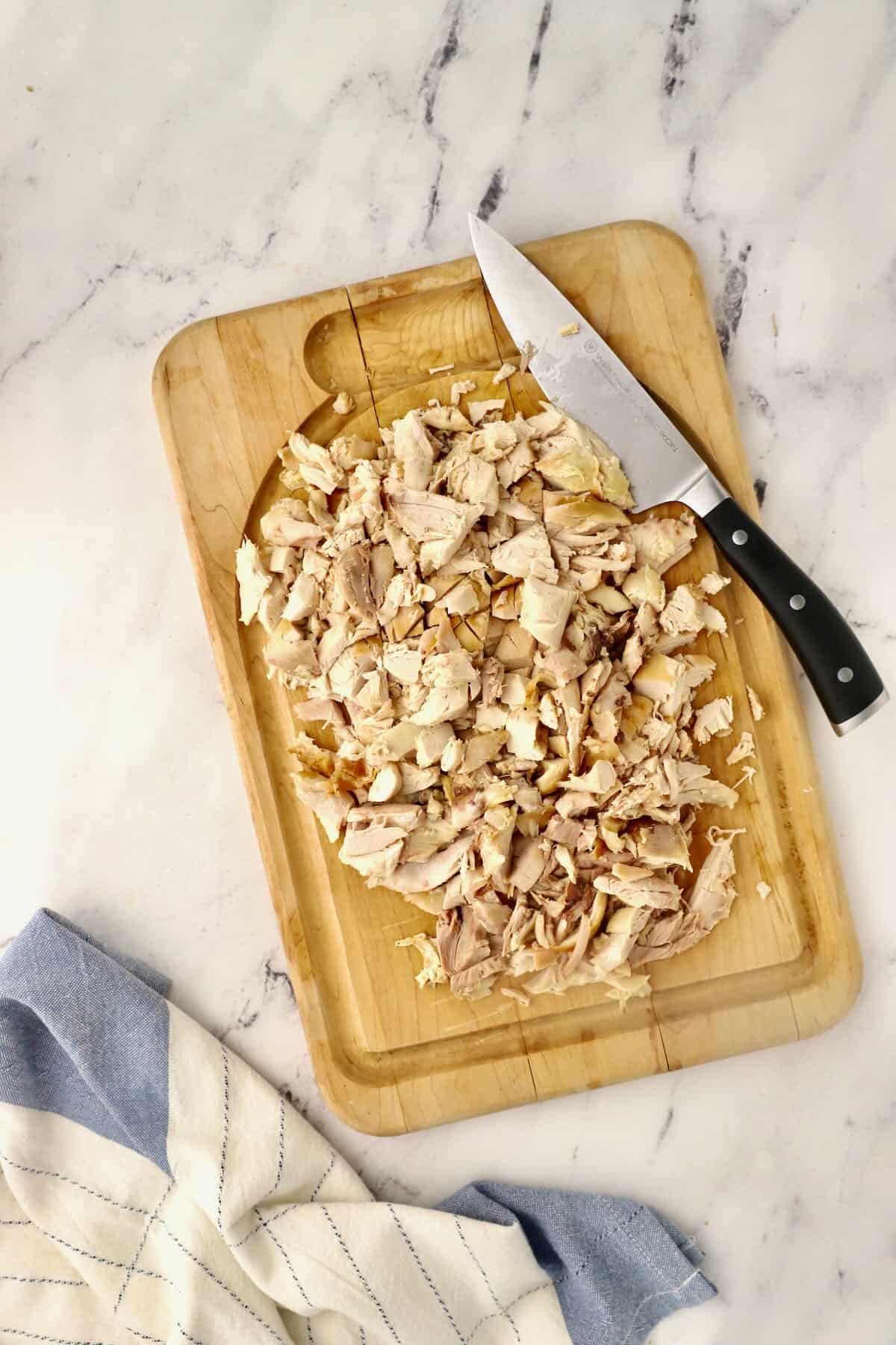 A cutting board with cut up chicken and a knife. 