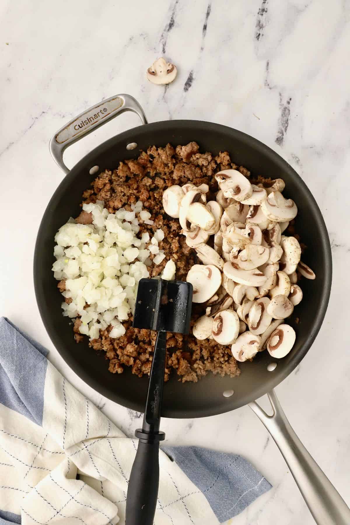 Sausage, mushrooms and onion cooking in a skillet. 