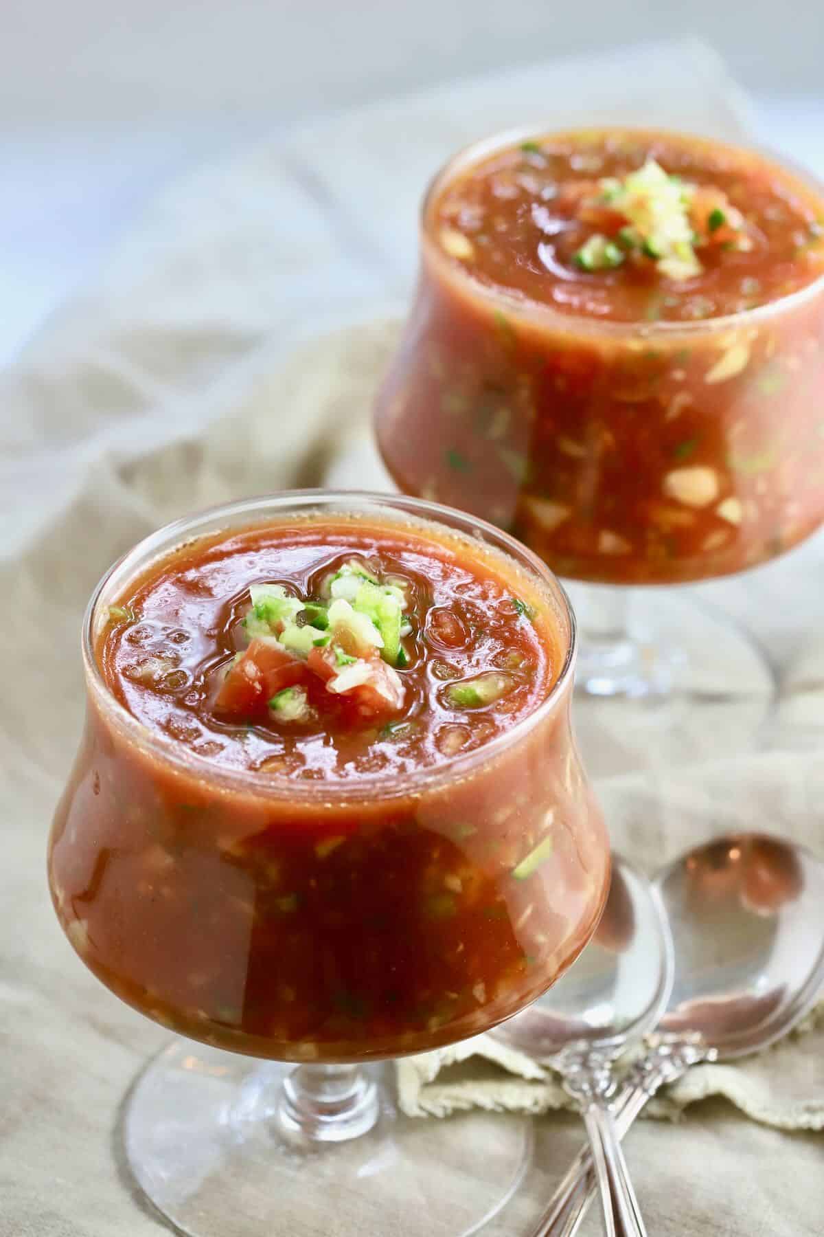 Two bowls of gazpacho topped with chopped cucumber. 