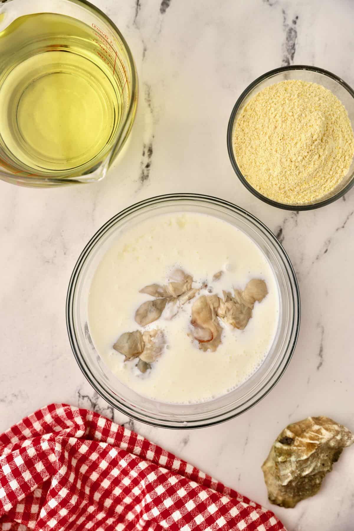 A clear glass bowl full of buttermilk and raw oysters. 