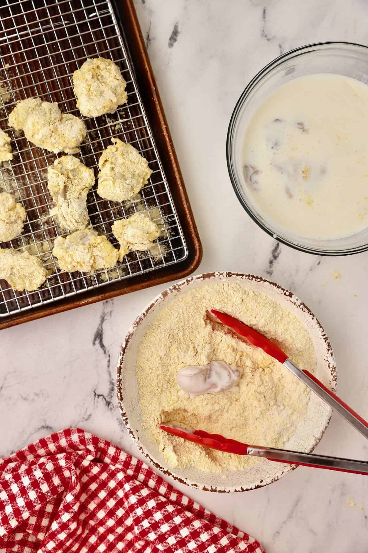 Using kitchen tongs to dredge an oyster in cornmeal. 