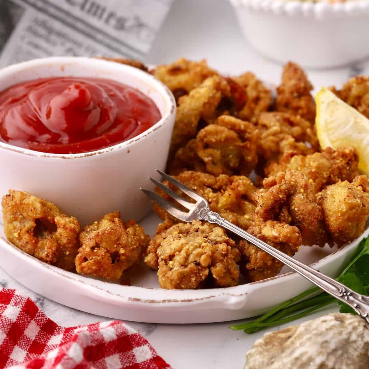 A plate of fried oysters with a bowl of cocktail sauce and cocktail fork.