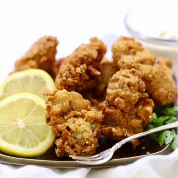 Fried oysters on a bronze plate garnished with lemon slices.
