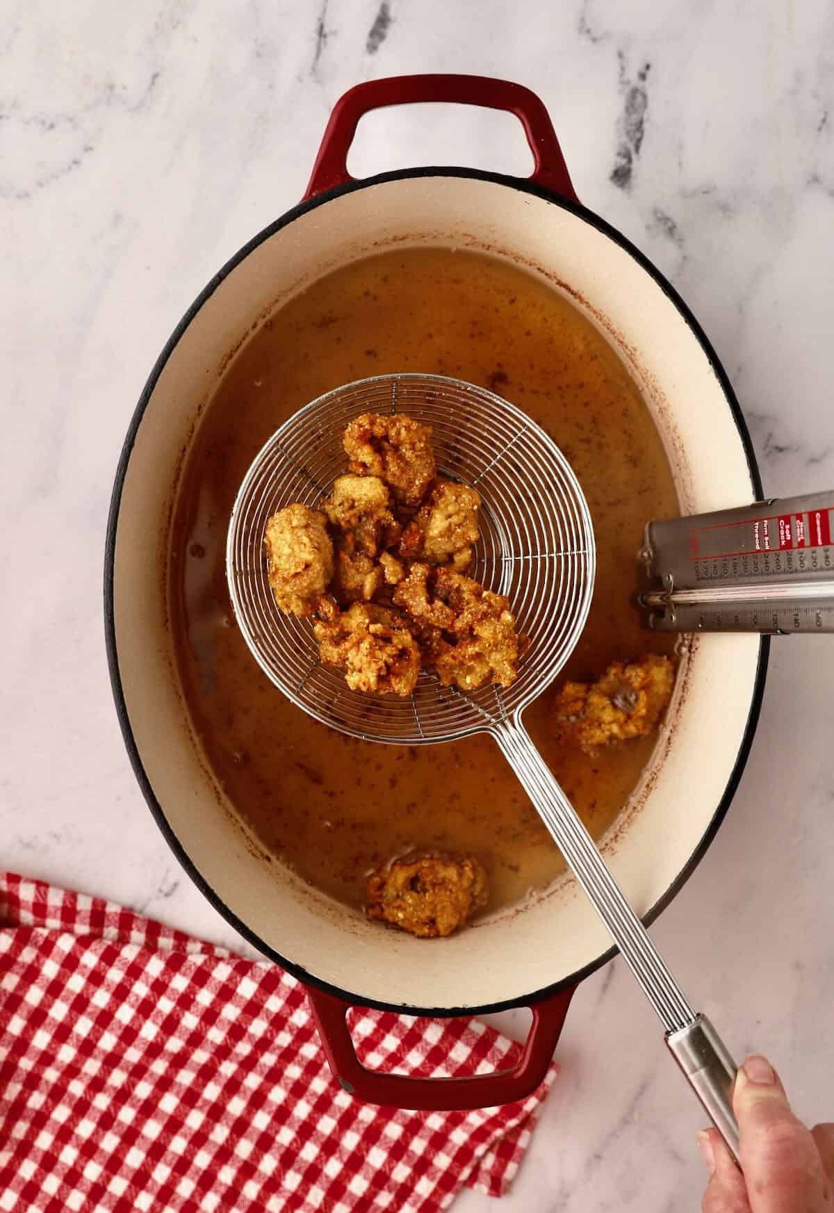 Fried oysters draining in a metal kitchen spider.