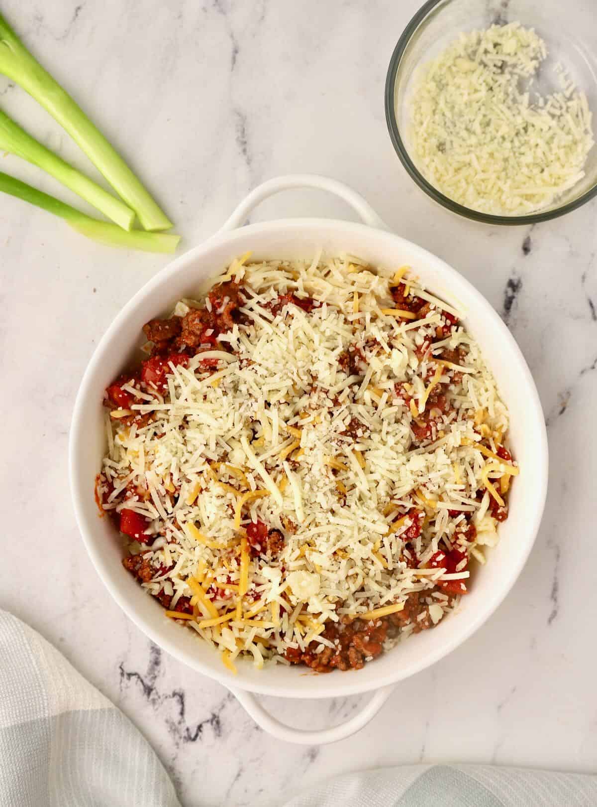 A beef noodle casserole topped with shredded cheese in a baking dish. 