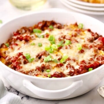 Hamburger noodle casserole in a white baking dish garnished with chopped scallions.