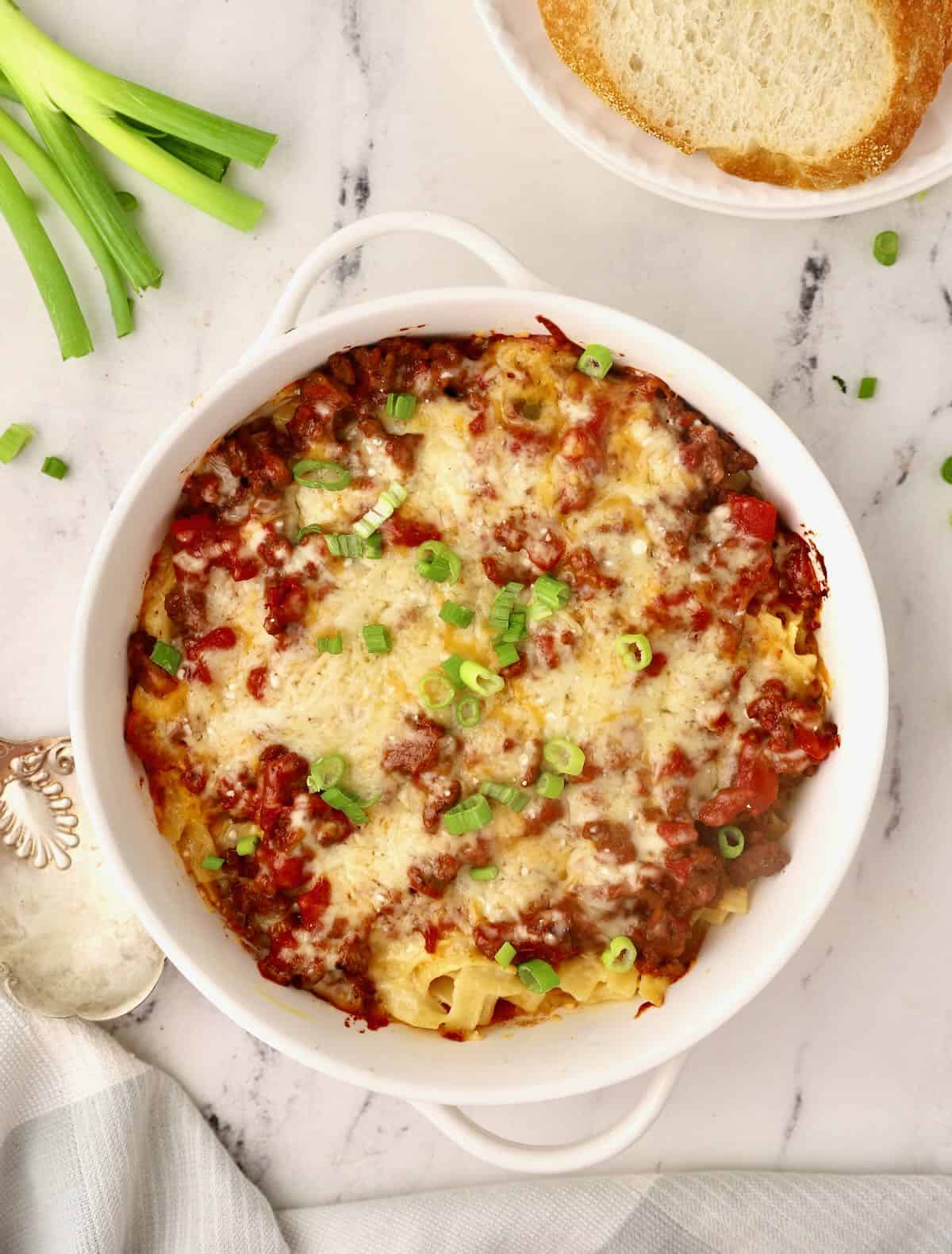 A white baking dish with hamburger noodle casserole garnished with chopped scallions.