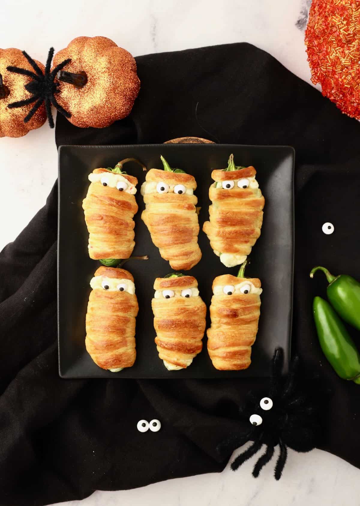 Halloween jalapeno mummies on a black plate.