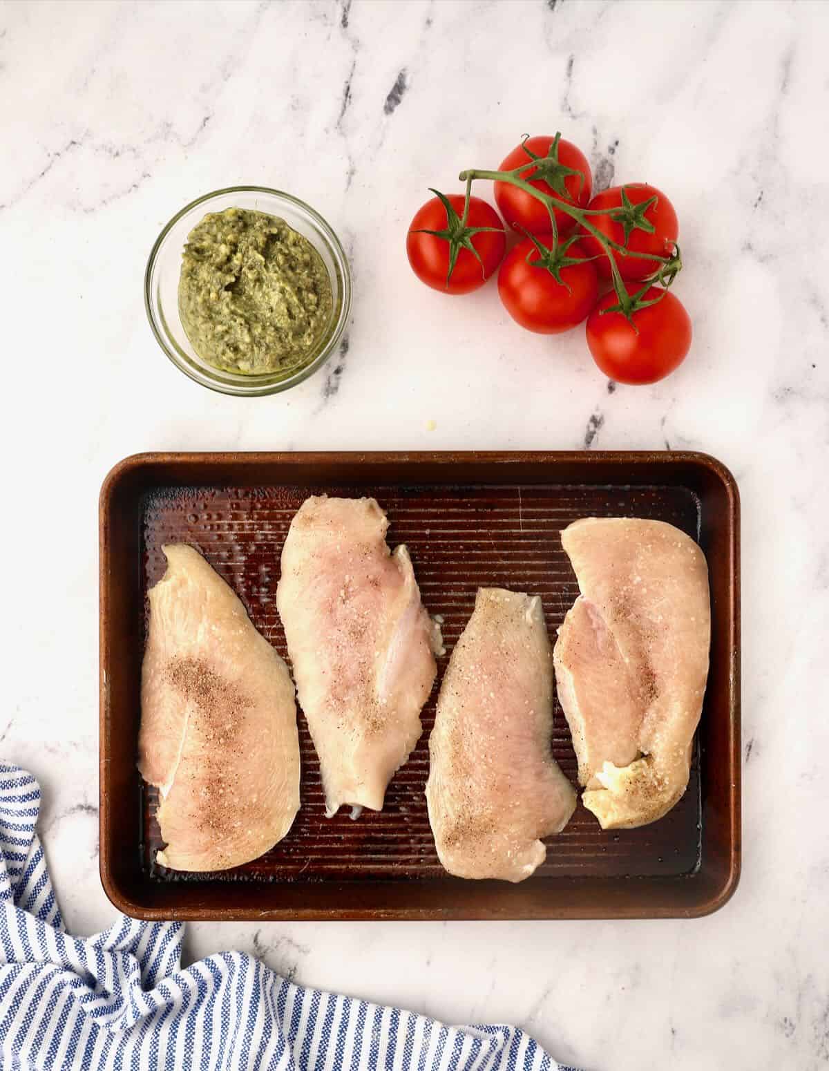 Four chicken breasts on a baking sheet. 