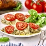 Two baked chicken breasts topped with pesto, mented mozzarella, and sliced tomatoes to make Chicken Pesto with Mozzarella.