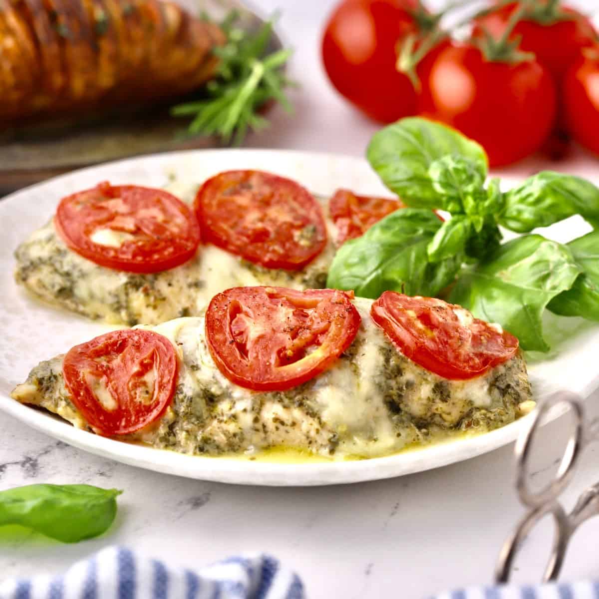 Two pesto chicken breasts on a plate topped with sliced tomatoes.