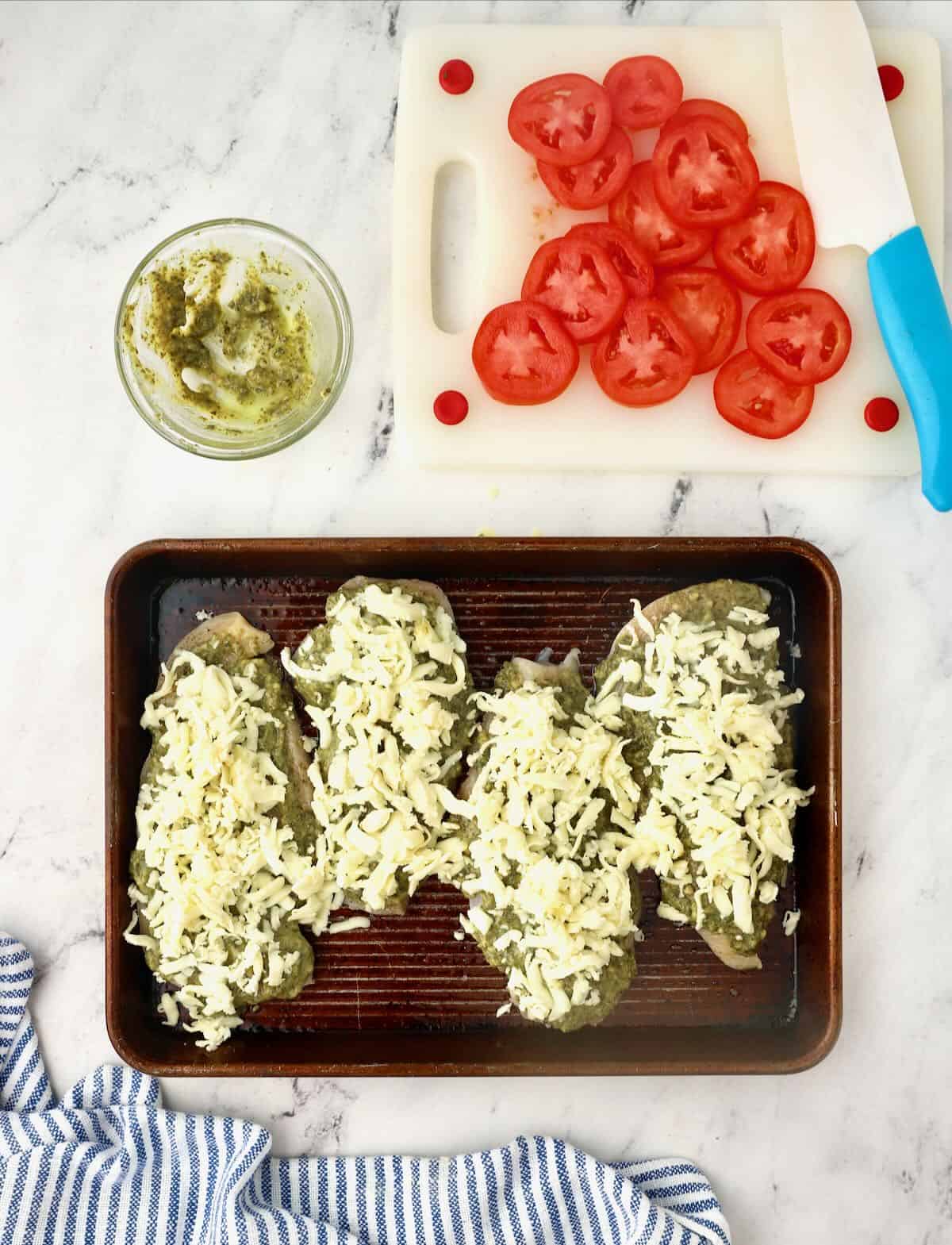 Four chicken breasts topped with pesto and cheese. 